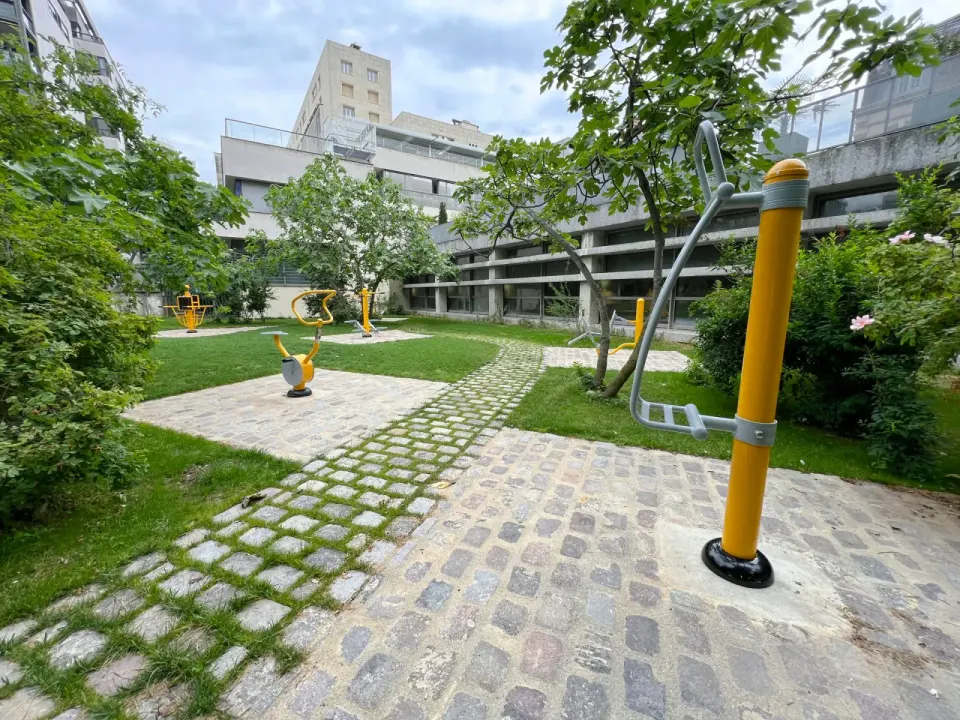 Espace de fitness extérieur Herkules Fitness dans le jardin arboré d'un site d'entreprise : vélo, appareils de cardio et de renforcement jaunes posés sur des pavés