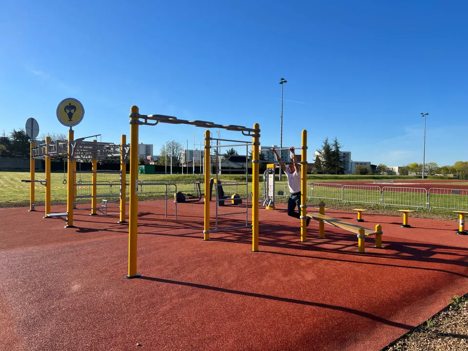 Homme suspendu à la barre de traction d'une station de street workout Herkules Fitness, au bord d'une piste d'athlétisme à Grand Angoulême